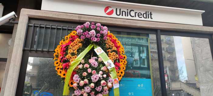 Due corone di fiori davanti l'Unicredit a Catania, è sfida bitcoin