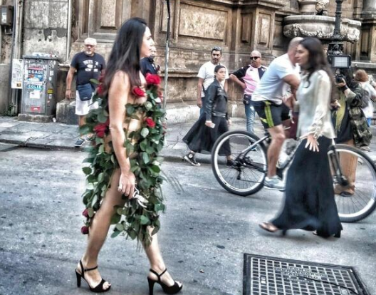 Un'artista vestita con sole rose rosse gira per le strade di Palermo